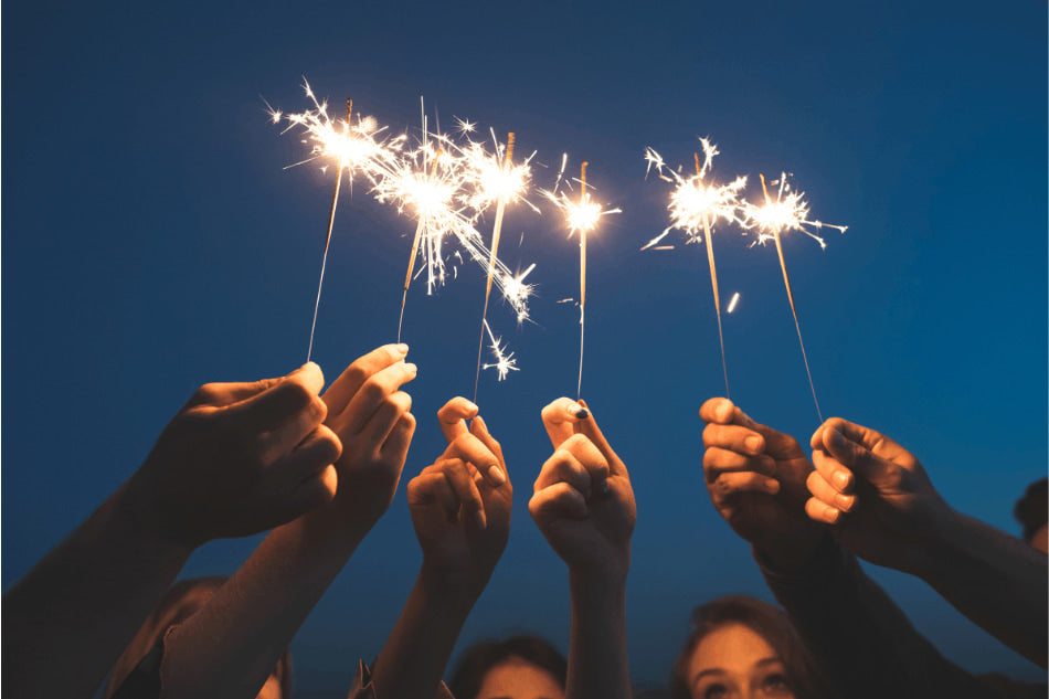 Pessoas segurando velas de faísca ao entardecer, celebrando o Ano Novo.
