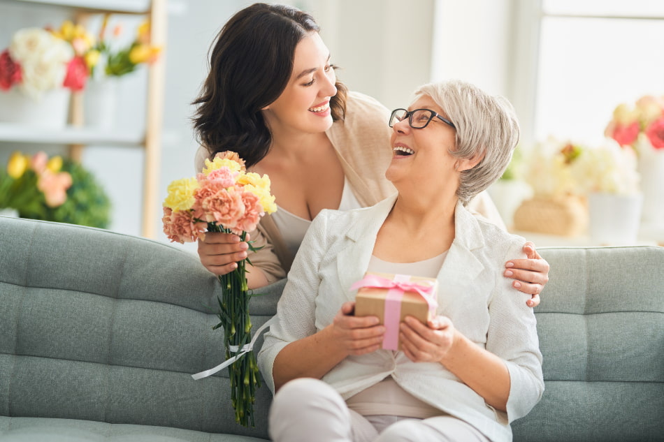 Mulher presenteando outra mulher com flores e um presente, celebrando momentos especiais