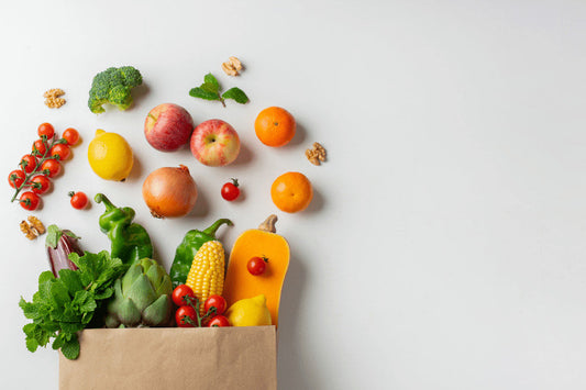 Sacola de papel com frutas e vegetais frescos, como tomates, maçãs, laranjas, milho e brócolis, sobre fundo branco.