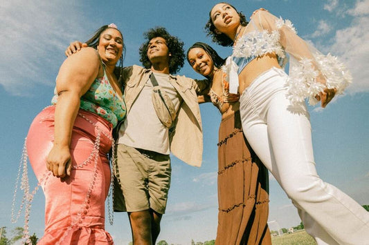 Grupo de pessoas com looks primavera com tons neutros e vibrantes misturados, ao ar livre, sob um céu azul.