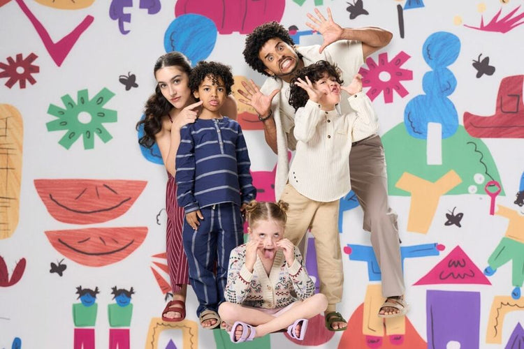 Adultos e crianças fazendo caretas juntos em frente a um painel colorido, representando como se divertir nas férias