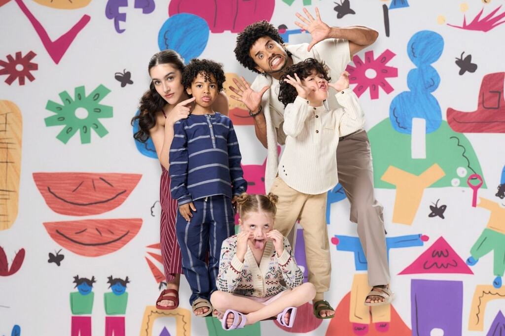 Adultos e crianças fazendo caretas juntos em frente a um painel colorido, representando como se divertir nas férias