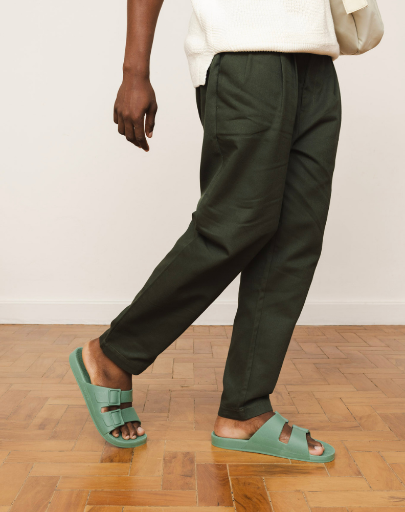 Pessoa caminhando veste Sandália Linus cor menta, com calça escura e fundo neutro, feita de material 100% reciclável.