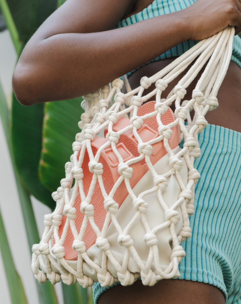 Pessoa com bolsa de macramê carrega Sandália Linus cor coral, feita de material 100% reciclável.