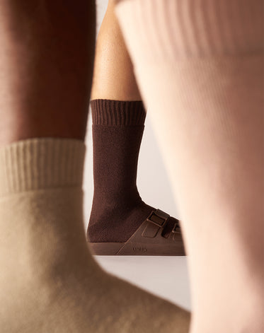 Parte inferior de três pernas usando meias e sandália Linus nas cores marrom escuro, médio e claro.