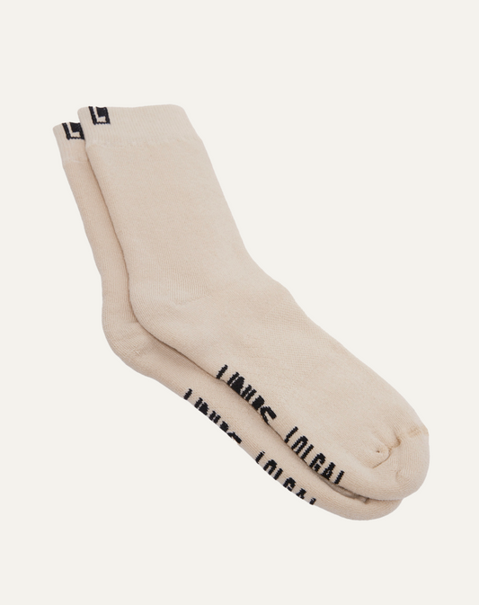 Par de meias de algodão na cor off white. Sola bordada com as palavras "LINUS" e "OLGA". Fundo da imagem em cinza claro.