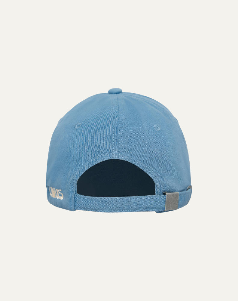 Boné em algodão na cor azul claro com bordado escrito versão brasileira em off white, vista traseira com ajuste em metal. Fundo da imagem em cinza claro. 