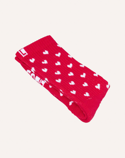 Meia de algodão com estampa de corações vermelho e branco vista dobrada com fundo cinza claro.