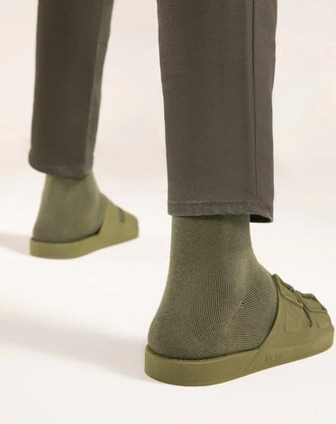 Parte inferior de duas pernas vistas de trás com calça verde usando meias e sandália na cor verde musgo da marca Linus.