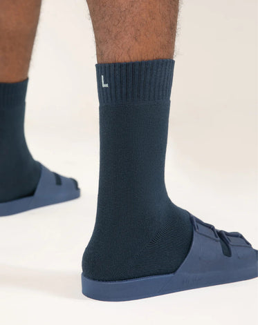 Parte inferior de duas pernas vistas de trás usando meias e sandália na cor azul da marca Linus. 