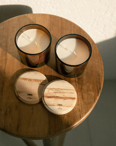 Mesinha de madeira com  duas velas em copos e suas tampas ao lado escritas "Fim de tarde" e "Picnic" da marca Linus Cosi.